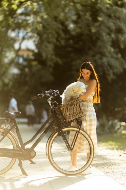 Jovem com cachorro branco bichon frise na cesta de bicicleta elétrica