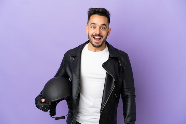 Jovem com capacete de motociclista isolado em um fundo roxo com expressão facial surpresa