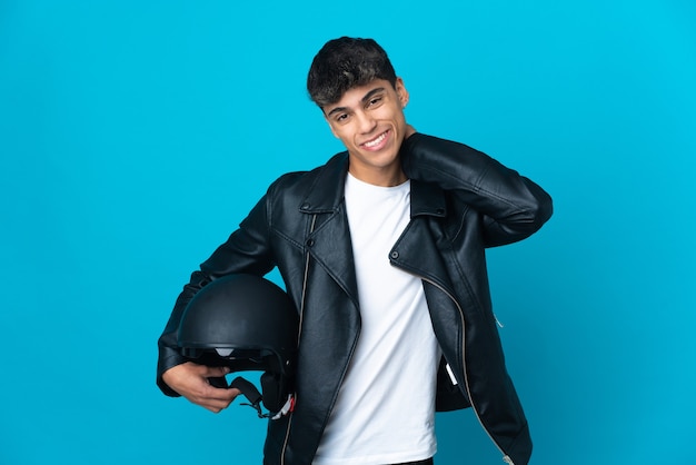 Jovem com capacete de motociclista sobre fundo azul isolado rindo