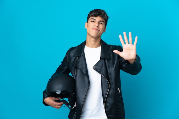 Jovem com capacete de motociclista sobre o azul isolado contando cinco com os dedos