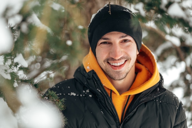 Jovem com capuz e jaqueta quente em um parque nevado e sorrindo