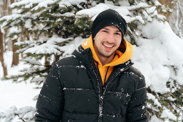 Jovem com capuz e jaqueta quente em um parque nevado e sorrindo