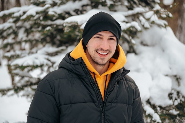 Jovem com capuz e jaqueta quente em um parque nevado e sorrindo