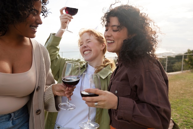 Foto jovem com chapéu de festa sorrindo e brindando com suas amigas durante a festa ao ar livre