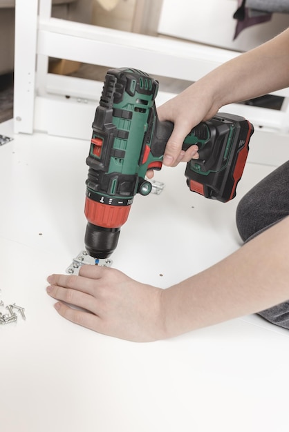 Jovem com chave de fenda sem fio montando mesa dobrável branca no chão