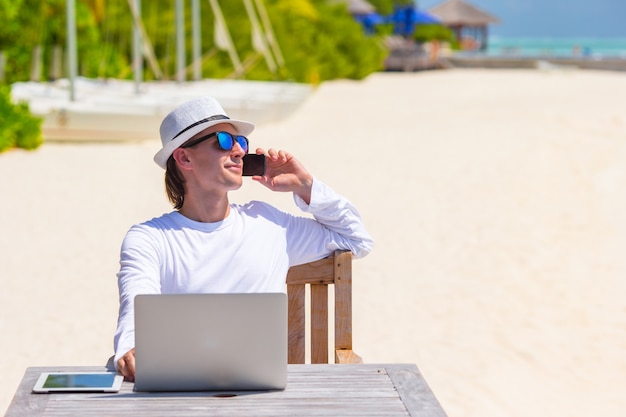 Jovem com computador tablet e celular na praia tropical