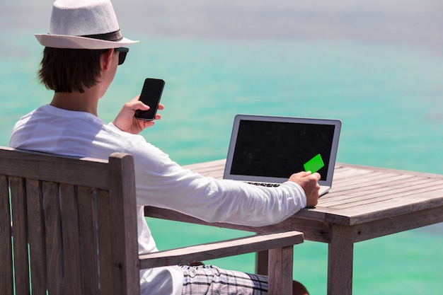 Jovem com computador tablet e celular na praia tropical