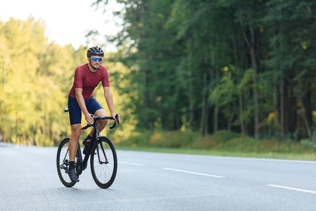 Foto jovem com corpo atlético, andar de bicicleta na estrada entre a floresta verde.