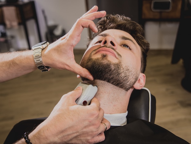 Jovem com corte de cabelo na moda na barbearia. O barbeiro faz o penteado e a barba.