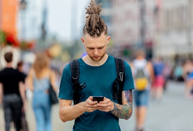 Jovem com dreadlocks andando com um telefone na rua