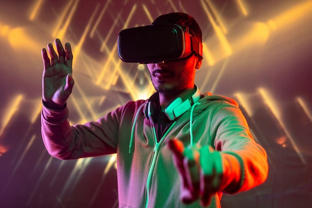 Jovem com fones de ouvido ao redor do pescoço gesticulando com as mãos enquanto obtém experiência de realidade virtual contra um fundo geométrico luminoso