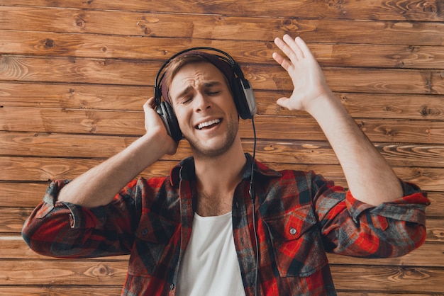 Jovem com fones de ouvido cantando na parede de madeira