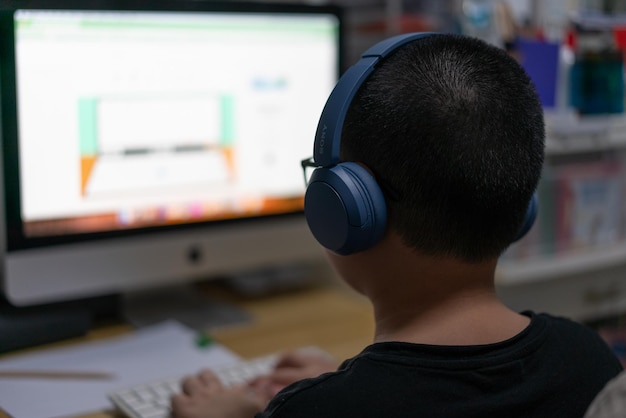 jovem com fones de ouvido ouvindo a lição da escola em casa no computador via internet