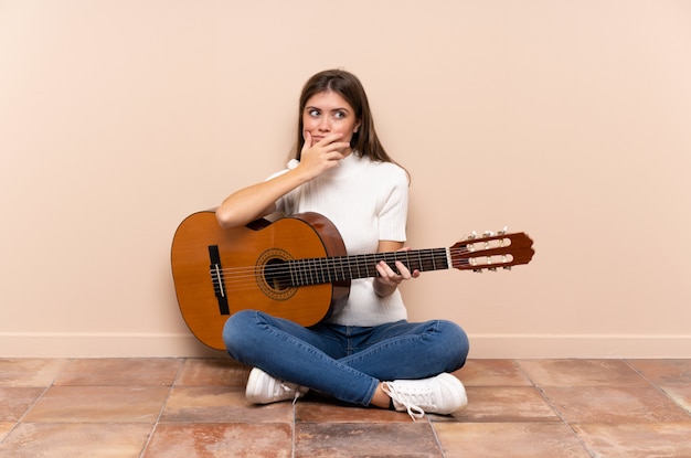 Jovem com guitarra sentada no chão pensando em uma ideia