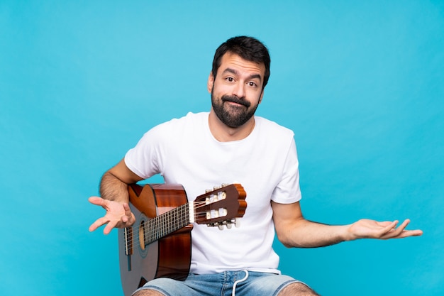 Jovem com guitarra sobre azul fazendo gesto de dúvidas