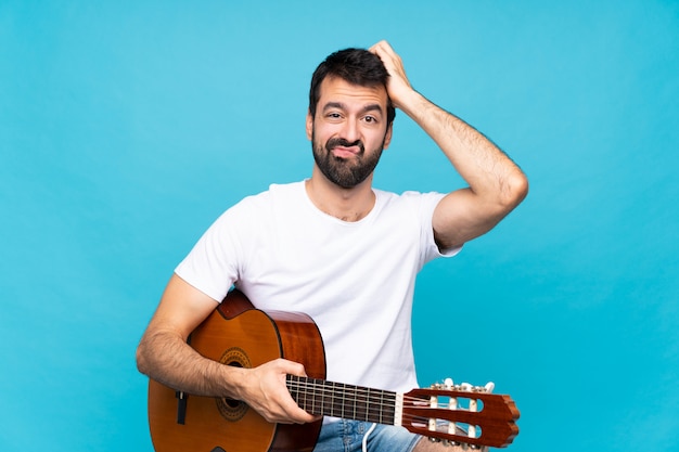 Jovem com guitarra sobre azul isolado com uma expressão de frustração e não compreensão