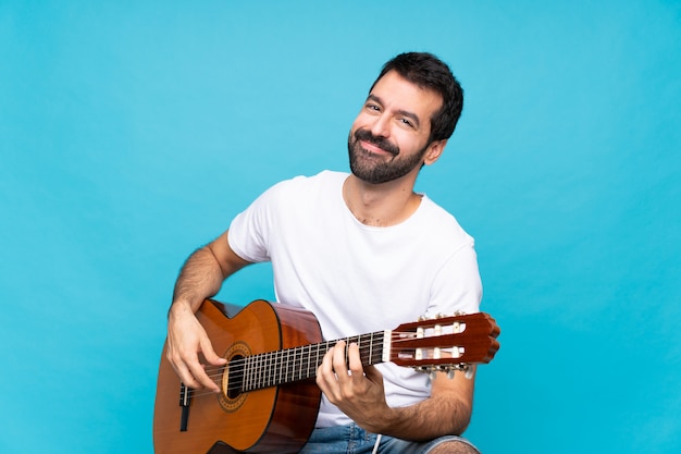 Jovem com guitarra sobre isolado azul sorrindo