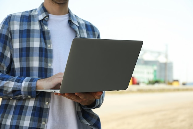 Jovem com laptop contra silos de grãos. negócios agrícolas