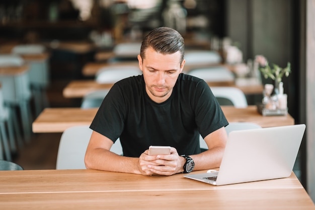 Jovem com laptop no café ao ar livre, bebendo café.