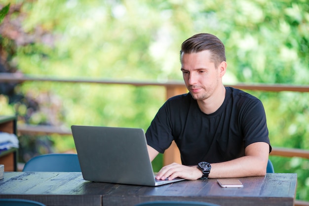 Jovem com laptop no café ao ar livre, bebendo café.