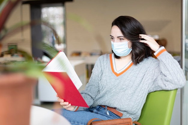 Jovem com máscara facial lendo um livro no espaço público Espaço para texto