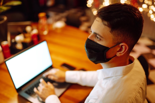 Jovem com máscara facial protetora trabalhando no laptop em casa durante as férias de inverno