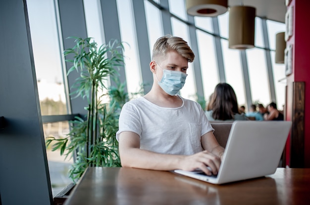 Jovem com máscara médica trabalhando em um laptop em um café