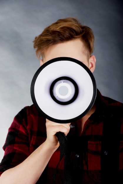 Jovem com megafone de pé contra um fundo cinzento