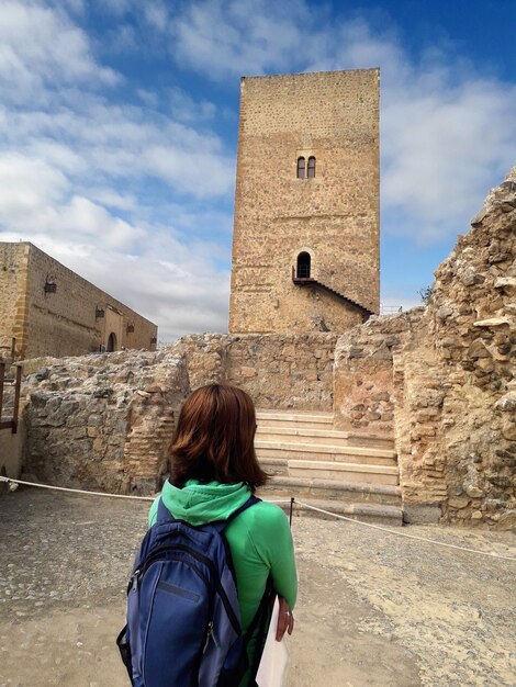 jovem com mochila azul olhando para a torre de um castelo