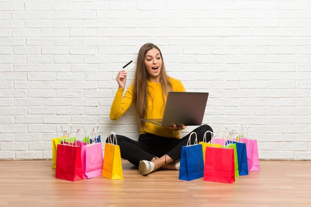 Jovem com muitos sacos de compras com laptop e cartão de crédito