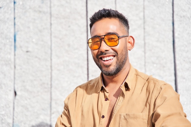 Jovem com óculos de sol laranja e barba sorrindo homem latino olhando para a câmera com dentes perfeitos