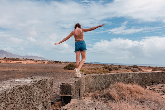 Jovem com os braços estendidos equilibrando-se em uma parede de pedra em um dia ensolarado