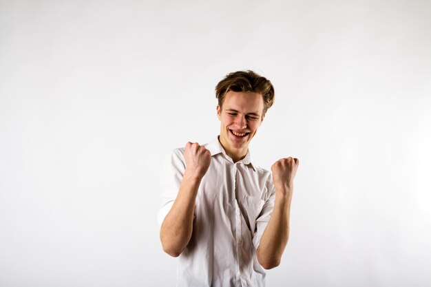 Jovem com os olhos fechados fazendo gestos enquanto celebra o sucesso contra um fundo branco