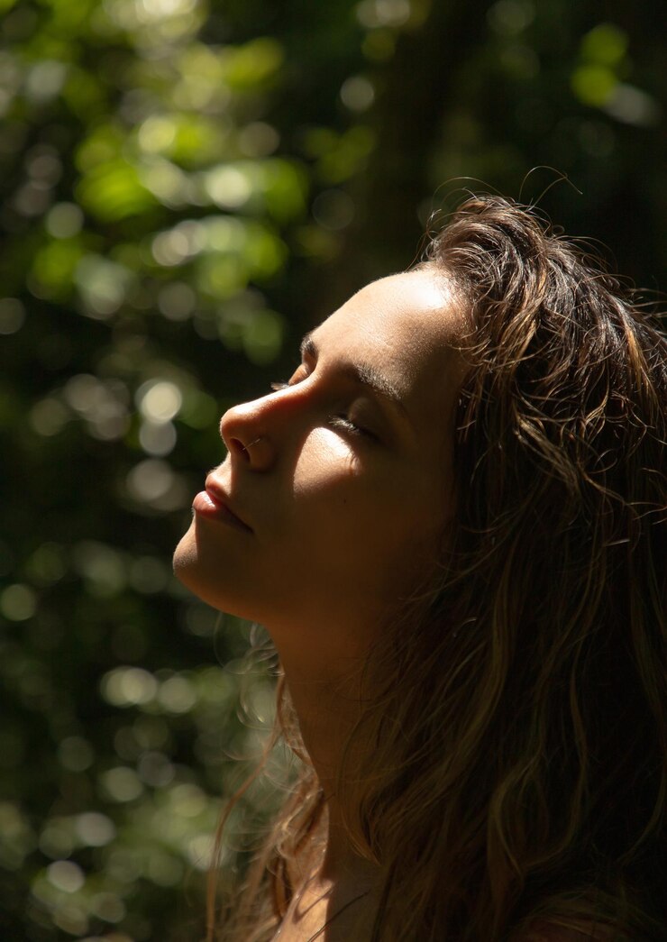Foto jovem com os olhos fechados iluminada pelo sol no meio da natureza