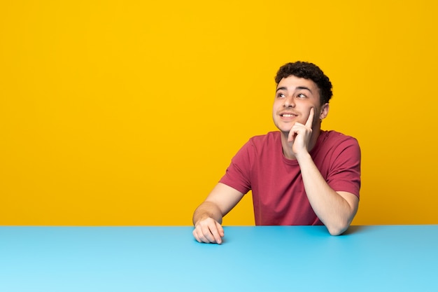 Jovem com parede colorida e mesa pensando uma idéia enquanto olha para cima