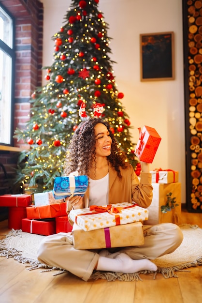 Jovem com presentes de Natal em casa perto da árvore de Natal Feriados de inverno Ano Novo