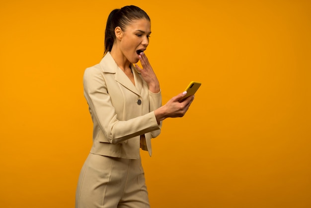 Jovem com problemas de pele facial, posando com um smartphone em um fundo amarelo.