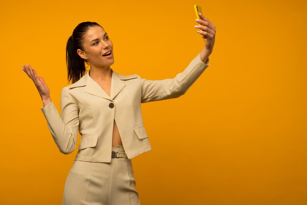 Jovem com problemas de pele facial, posando com um smartphone em um fundo amarelo.