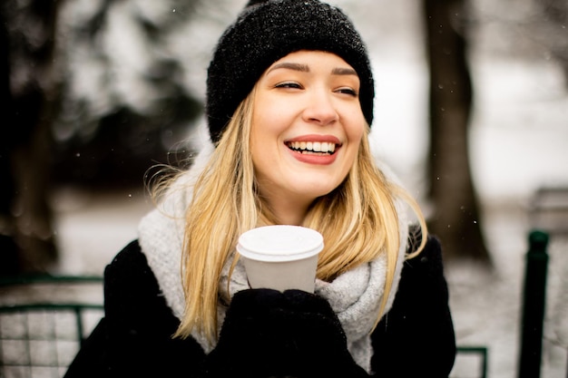 Jovem com roupas quentes desfrutando na neve com uma xícara de café para viagem