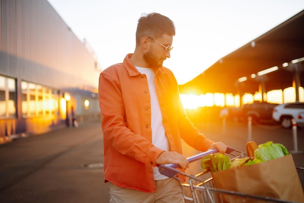 Jovem com sacola de compras cheia de legumes perto do carro Homem bonito depois das compras