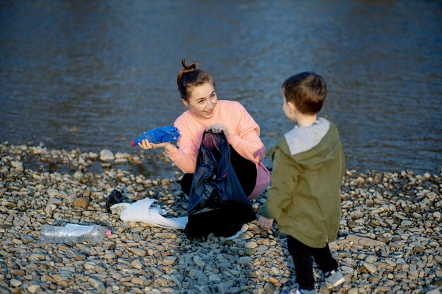 Jovem com seu filho coleta lixo plástico em um saco de lixo no rio Garrafas plásticas sujas vazias usadas Costa de poluição ambiental