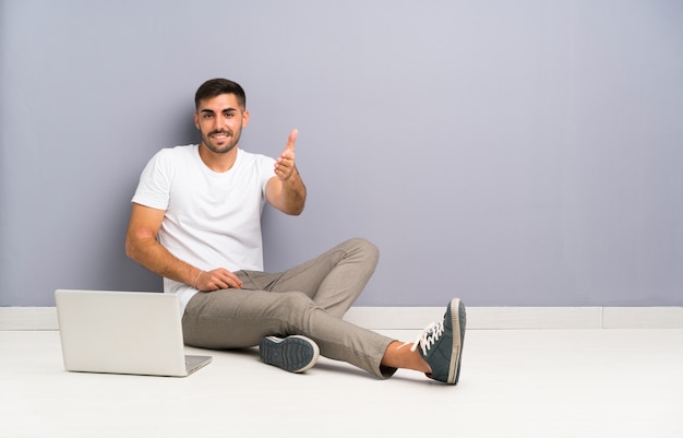 Jovem com seu laptop sentado um aperto de mão no chão depois de um bom negócio