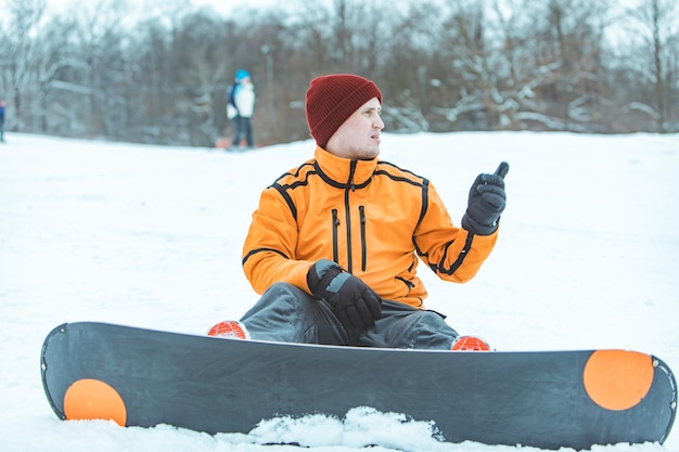 Jovem com snowboard descansando sentado na neve