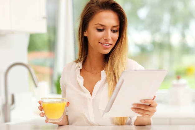 jovem com suco de laranja e tablet na cozinha