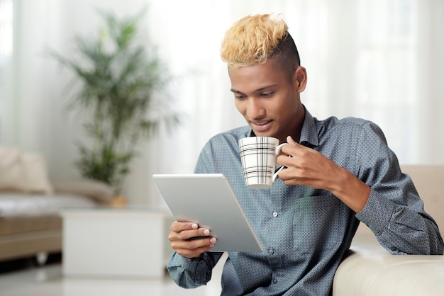 Jovem com tablet digital tomando café da manhã e lendo notícias