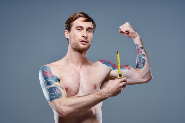 Jovem com tatuagem e fita métrica músculos inflados modelo de fisiculturista fitness