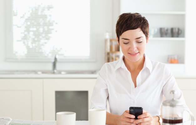 Jovem com telefone celular e café na cozinha