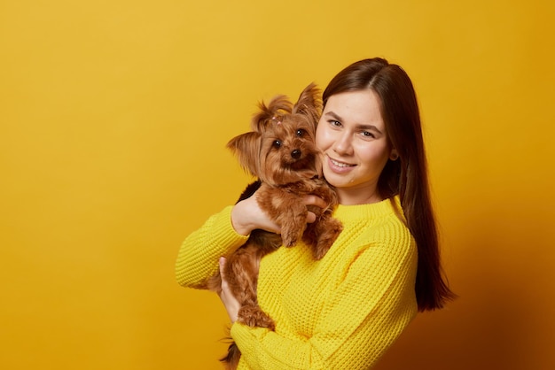 jovem com um cachorro Yorkshire terrier em um fundo amarelo limpo