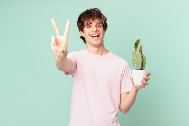 Jovem com um cacto sorrindo e parecendo feliz, gesticulando vitória ou paz