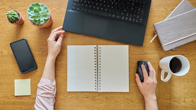 jovem com um caderno aberto usando um laptop em uma mesa de madeira